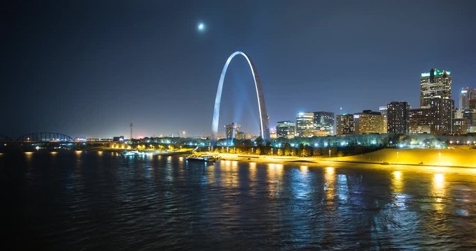 St. Louis, Missouri, USA - view of the illuminated city at night with the Gateway Arch monument and the Mississippi River with passing ship - Timelapse with zoom out 