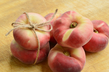 Dough nut peaches also known as Saturn peach with hemp rope  on wooden board.
Benefits of Dough nut peaches.