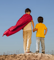 Obraz na płótnie Canvas Two boys playing superheroes on the sky background