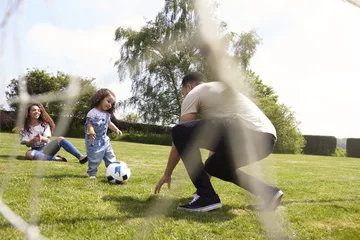 Tuinposter Parents squat to play football with their young daughter © Monkey Business
