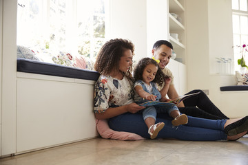Parents and their daughter sitting on the floor reading book