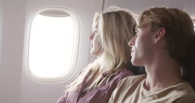 Attractive young couple look out of the window while flying in main cabin of commercial jet airliner. Close up profile shot, recorded hand-held at 60fps