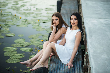 mother and daughter in white dresses sitting on a pier summer the evening