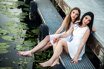 mother and daughter in white dresses sitting on a pier summer the evening