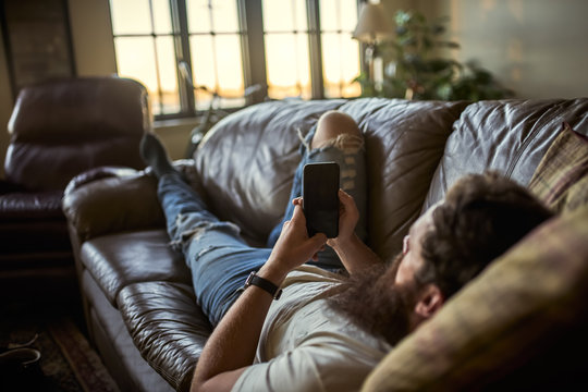 Bearded Guy Relaxing On Couch At Home Using Smart Phone