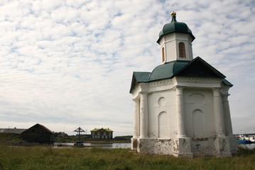 Fototapeta na wymiar Alexander chapel on the shore of the bay of Wellbeing and Memorial cross at Solovki islands in White sea, Russia
