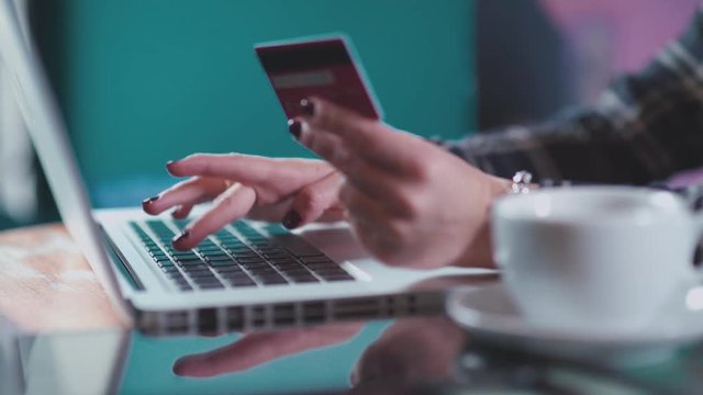 Online shopping: woman makes an online purchase with a credit card and a laptop sitting in a cafe. Laptop and cup of tea on the table. A woman makes a purchase with a cup of tea in the online shop