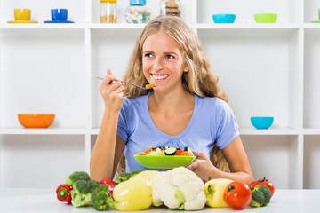 Obraz na płótnie Canvas Beautiful girl enjoys eating vegetable salad at her home. 