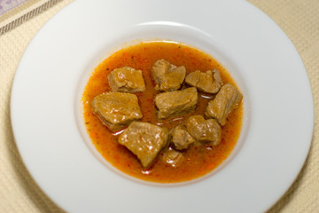 Pieces of meat in tomato sauce on a plate. Delicious meat in a sauce on a white plate.