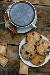 Beautiful concept. Chocolate cookies on a white plate on a wooden background and tea. Nearby stands a Christmas tree, toys, garlands and Christmas toys.