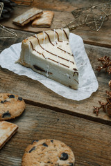 Beautiful homemade cake cheesecake on a white paper on the wooden background. Next chocolate chip cookies, Christmas gifts, Christmas tree, cones and toys. Conceived to celebrate the new year.