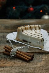 Beautiful homemade cake cheesecake on a white paper on the wooden background with cinnamon stick. Near Christmas gifts, Christmas tree and toys. Conceived to celebrate the new year.