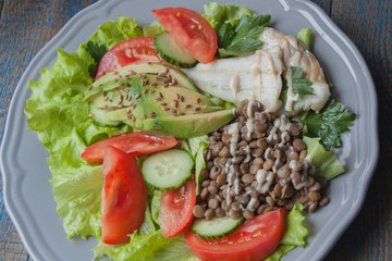 Healthy green salad with boiled cod fish, lentils, tahini, parsley, tomatoes, cucumbers, avocados, flax seeds on a large gray plate. Love for a healthy raw food concept