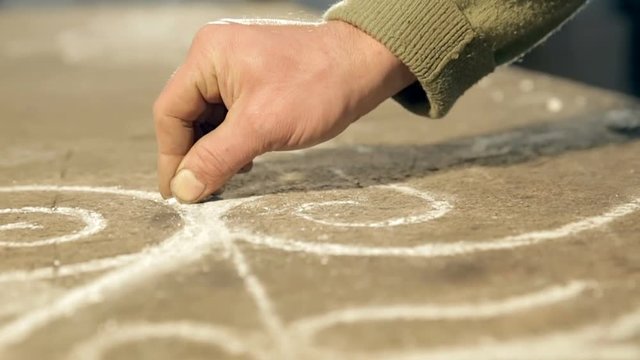 Close-up hand of the artist who draws with chalk sketch on plywood