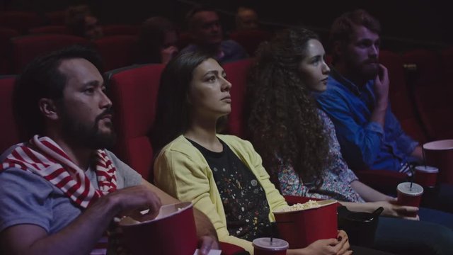 People sitting with popcorn and drinks and watching movie in film theater 