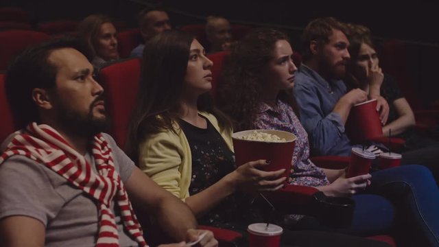 Concentrated people watching movie in cinema theater and eating popcorn