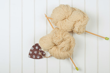 Natural woolen yarn with wood needles on white wooden background.