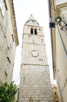 The renaissance bell tower of the Parish Church of the Assumption of the Blessed Virgin Mary in Vrbnik town, Krk, Croatia. A medieval spire with a clock and historic religious monument and landmark.