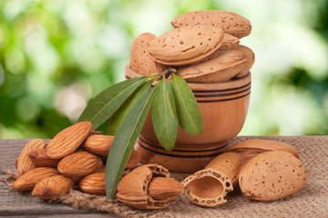 almonds with leaves in a bowl on the old wooden board  blurred garden background