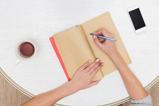 Female designer hands holding cup of hot beverage and working with notebook. Employee woman drinking morning tea of coffee. Coffeebreak during working day, advertising business concept
