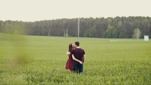 Man and woman in love. Couple walking in an oat field, kissing, hugging. Woman in red dress touches man s face. Slow mo