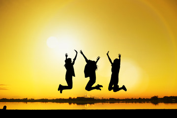 silhouette of young girl friends jumping with joy at sunrise or