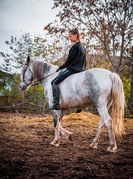 Young beautiful brunette girl rides a horse on a warm and sunny autumn day. Portrait of a pretty young woman on the horse, wearing tall boots and gloves.