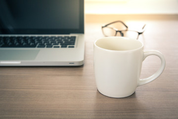 Close up view of a work desk interior with a laptop computer, A coffee cup on working table with glass. Vintage tone photo of work desk with computer and coffee cup
