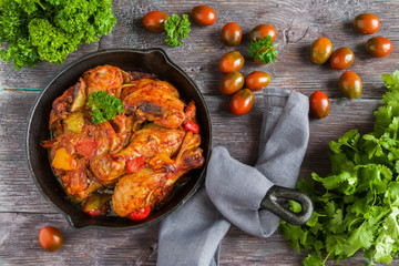 Chakhokhbili, chicken stew, cooked with tomatoes, bell peppers, spices and herbs. Dark wooden background, top view.