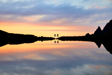 Fototapeta na wymiar Couple jumping near by lake in mountains during beautiful summer sunrise.