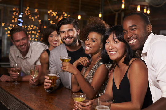Young adult friends by the bar at a party looking to camera