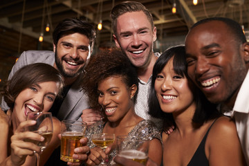 Happy friends at a party in a bar look to camera, close up