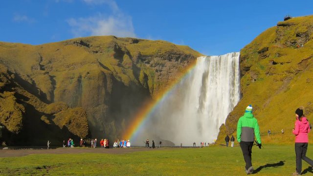 many tourists are walking and taking pictures near icelandic waterfall Skogafoss and rainbow