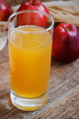 Glass of apple juice and red apples on wooden background