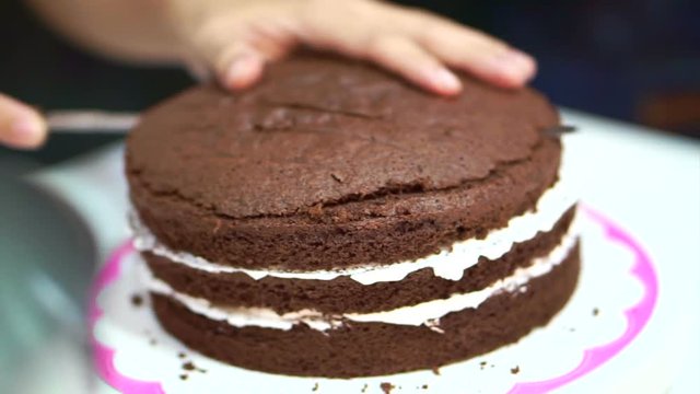 Patisserie chef baking decorating chocolate sponge cake. Putting white cream in the middle layers
