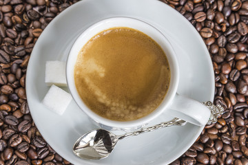 White cup of coffee on coffee beans. Top view