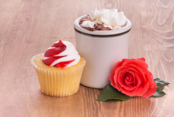 Strawberry cupcake with a cup of hot chocolate and a bright red rose on dark wooden tabletop - anniversary or Valentine's treat to a loved one