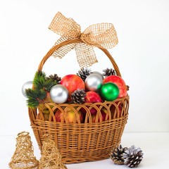 the red apples, pine cones and decorative balls in wicker brown basket on a white background