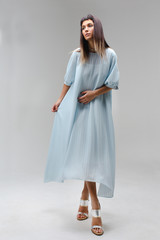 Woman make step in light long blue dress in studio