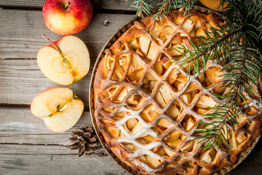 Traditional american apple pie on rustic wooden table, with apple. Near the Christmas tree branches and pine cones, top view