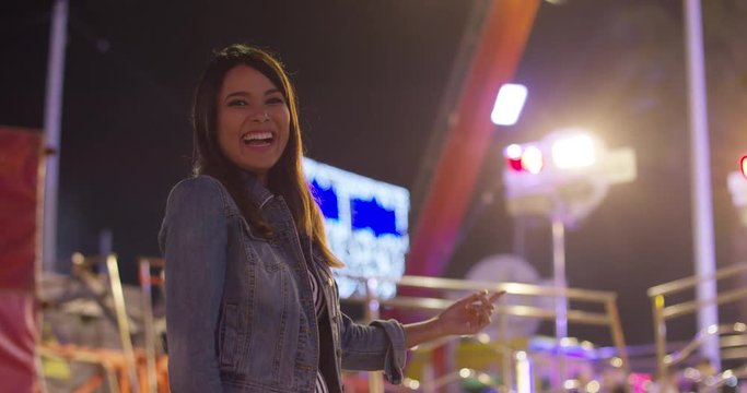 Vivacious young woman at an evening funfair standing laughing against a backdrop of colorful lights