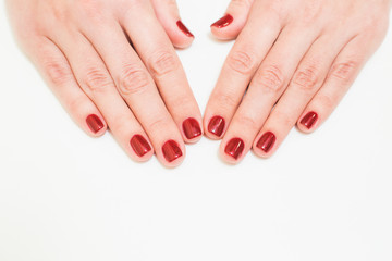 Close up of caucasian female hands with professional red manicure with glittering sparkles isolated on white background. Modern festive gel polish with base coat first and top cure with UV or LED lamp