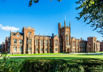 The Queen's University of Belfast with a grass lawn, tree branches and a hedge in sunset light - 127330898