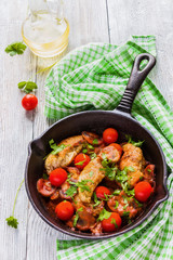 Roasted chicken fillet, cooked with mushrooms, garlic, paprika and olive oil. Cast-iron skillet and fresh cherry tomatoes on wooden table, top view.