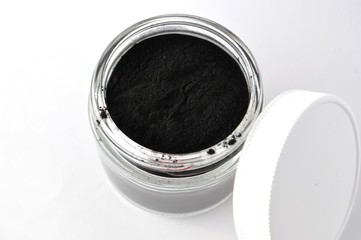 Activated charcoal powder for cosmetic face mask in a jar top view with copy space