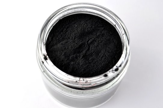 Activated charcoal powder for cosmetic face mask in a jar top view with copy space