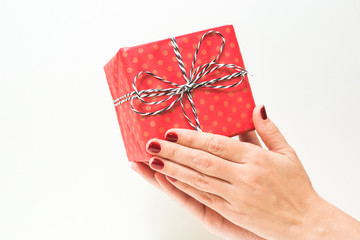 Woman with beautiful red manicure holding small present in hands. Close up of box in wrapping paper isolated on white background. Horizontal color photo.
