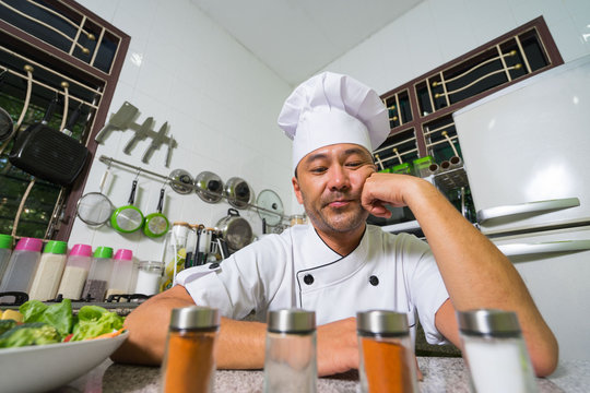 Asian chef sitting on the kitchen and thinking. In the front of picture  blured spices.