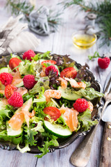 Fresh salad with smoked salmon, shrimps, raspberries and cherry tomatoes on white wooden background. Delicious Christmas themed dinner table