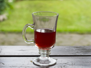 Red fruit tea in glass cup half-empty on wooden table, bokeh background, selective focus, shallow DOF